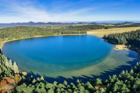 Vue aérienne du lac de Servièressurrounded par une forêt de pins. Le ciel est bleu clair avec quelques nuages.