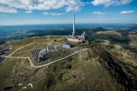 Vue aérienne du Puy de Dôme dans le Massif Central, avec sa tour de télécommunication et des parapentistes profitant du paysage.