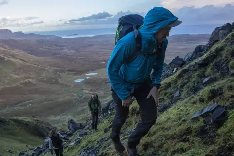 Randonneurs sur un sentier escarpé du Skye Trail, profitant d'un paysage spectaculaire avec des lacs et la mer en arrière-plan.