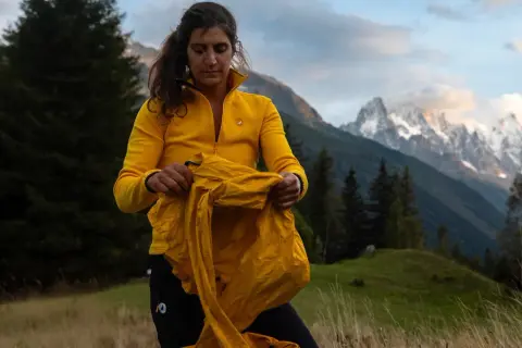 Une randonneuse en jaune prépare ses affaires, prête pour une aventure en montagne. Ses 3 couches randonnée sont essentielles pour affronter le climat changeant.