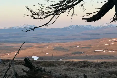 Vue panoramique depuis le Signal du Luguet, avec des montagnes enneigées à l'horizon et des collines dorées par le soleil couchant.