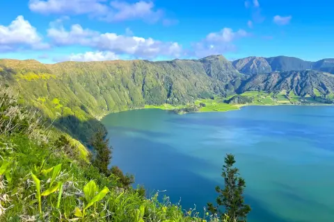 Vue panoramique sur le lac d'une beauté saisissante à São Miguel, entouré de montagnes verdoyantes sous un ciel bleu éclatant.