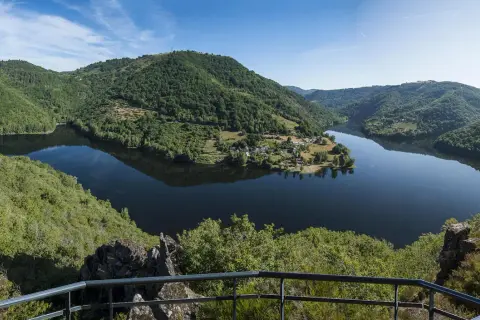 Vue panoramique des gorges de la Truyère, un lac paisible serpente entre des collines verdoyantes. Idéal pour la randonnée.