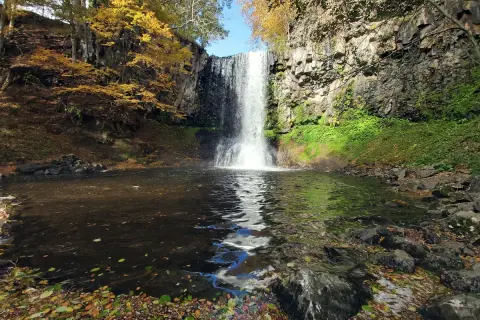 La cascade d'Entraigues, un rideau d'eau tombant dans un bassin entouré de roches et de feuillages d'automne aux couleurs vives.
