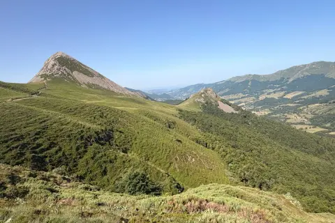 Vue panoramique sur le Puy Griou, sommet emblématique du Cantal, avec ses pentes verdoyantes et rocheuses sous un ciel bleu.