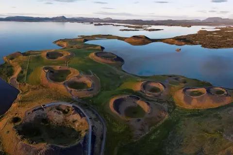 Paysage spectaculaire du lac Myvatn en Islande, avec ses cratères volcaniques verdoyants et ses eaux calmes reflétant le ciel.