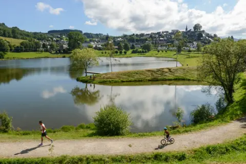 Un homme court sur le sentier, un enfant fait du vélo près du lac tour d'auvergne. Village en arrière-plan.