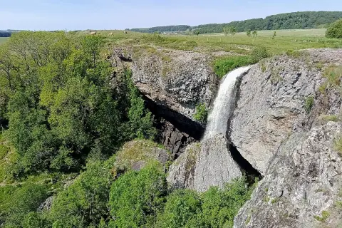 La cascade du Deroc, un lieu idéal pour la baignade, dévale une falaise rocheuse entourée de verdure.