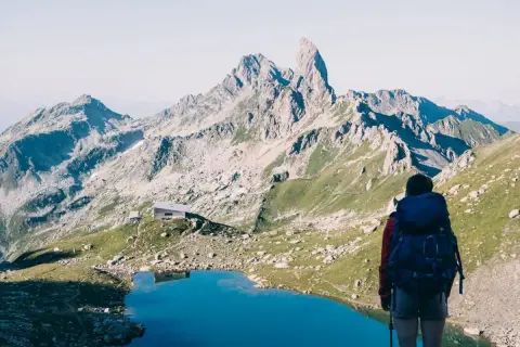 Randonneuse admirant un lac bleu et des montagnes majestueuses, un refuge en vue. Une belle étape du tour du Beaufortain 3 jours.