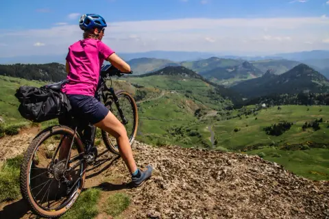 Cycliste au col de la Croix de Boutières, admirant le paysage verdoyant et vallonné. Sacoche sur le vélo, prête pour l'aventure.