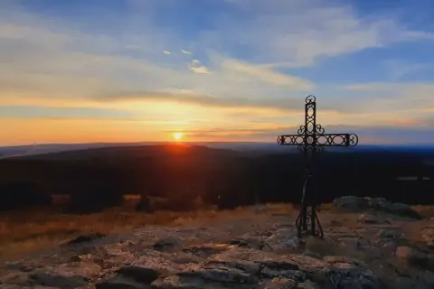 Coucher de soleil sur le moure de la Gardille, avec une croix ornementale veillant sur le paysage.