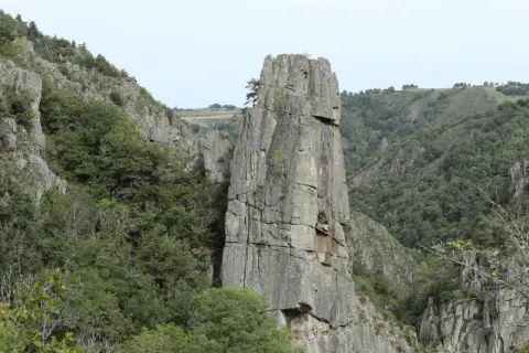 Un piton rocheux domine les gorges du Bes, entouré de végétation luxuriante et de falaises escarpées.