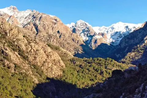 Paysage de Corse, entre mer et montagnes, idéal pour un séjour "mare e monti nord en 7 jours". Montagnes enneigées, rochers et pins.