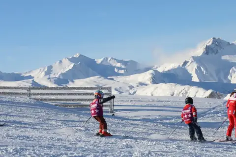 Enfants en plein cours de ski, profitant d'une journée ensoleillée avec des montagnes enneigées en arrière-plan.