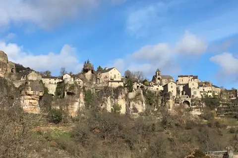 Village perché sur une falaise, un paysage typique du Cantobre Aveyron. Maisons de pierre, église et ciel bleu.