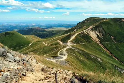 Sentier sinueux sur les pentes verdoyantes du Puy de Dôme, offrant une vue panoramique sur le village autour du Mont-Dore.