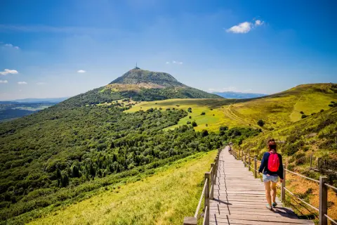 Une randonneuse sur un sentier en bois, profitant du paysage verdoyant du Massif Central. Le tourisme y est magnifique.