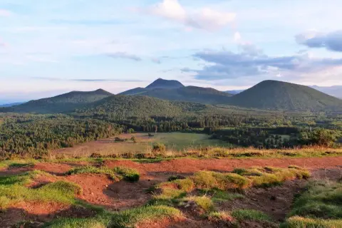 Vue panoramique sur les volcans d'Auvergne, avec le Puy Chopine dominant la forêt verdoyante sous un ciel nuageux.