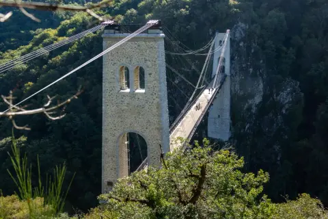 Le viaduc des Rochers Noirs, un pont suspendu impressionnant, traverse une vallée verdoyante. Deux personnes à vélo profitent de la vue.
