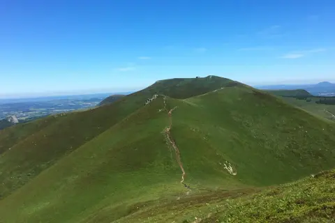 Sentier sinueux menant à la croix Morand, dominant un paysage verdoyant sous un ciel bleu.