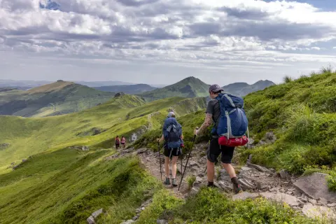 Randonneurs sur un sentier escarpé, dominant des paysages verdoyants et des volcans du puy May.