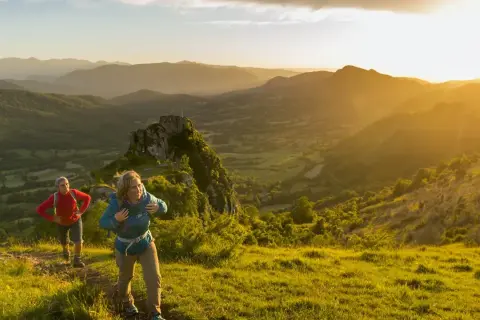 Deux randonneurs sur le sentier des cathares, profitant d'un paysage montagneux baigné par le soleil couchant.