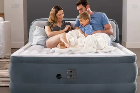 Famille heureuse sur un matelas gonflable, prêt à l'emploi grâce à un aspirateur.
