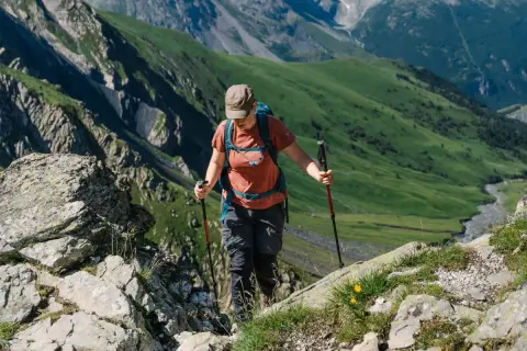Randonneuse utilisant des bâtons pour gravir une pente rocheuse. Ces bâtons de marche servent à stabiliser et soulager les articulations en terrain accidenté.