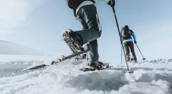 Deux personnes font une randonnée hivernale en raquettes sur un paysage enneigé sous un ciel bleu clair.