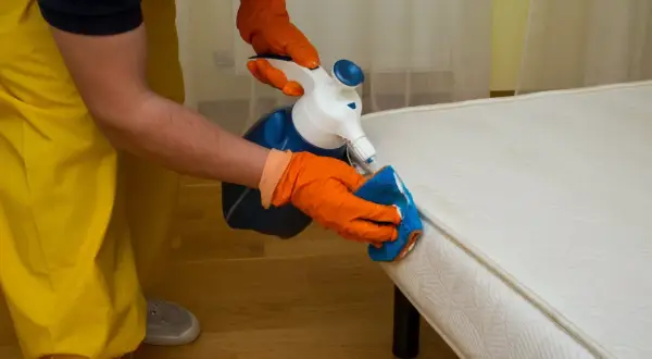 Personne en gants orange nettoie un matelas avec un spray et une éponge. Apprenez comment nettoyer un matelas gonflable efficacement.