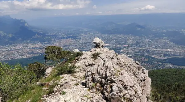 Vue panoramique depuis le sommet rocheux du Moucherotte, dominant une ville étendue sous un ciel bleu parsemé de nuages.
