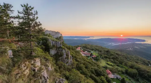 Vue panoramique d'un coucher de soleil sur la mer Adriatique, avec des ruines de château et des villages sur les pentes verdoyantes, sur le sentier Alpe Adria.