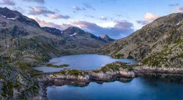 Vue aérienne du lac des 7 Laux, entouré de montagnes rocheuses et verdoyantes, sous un ciel aux teintes rosées.