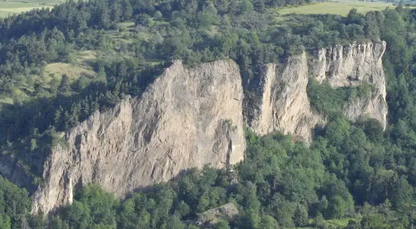 Falaises rocheuses spectaculaires, idéales pour une randonnée à Murol. Végétation luxuriante et paysage vallonné en arrière-plan.