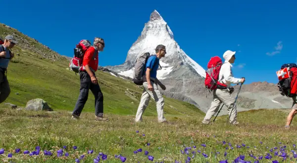 Randonneurs en marche avec le **Tour du Cervin** en toile de fond, sous un ciel bleu éclatant.