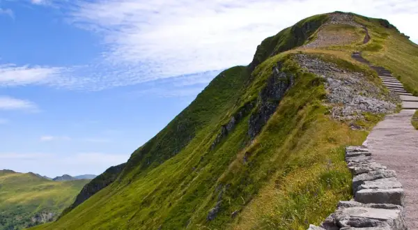 Sentier de montagne verdoyant avec escaliers, idéal pour une randonnée gr pour débutant. Paysage spectaculaire sous un ciel bleu.