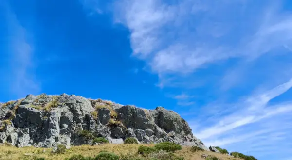 Rochers escarpés du Puy de Niermont sous un ciel bleu éclatant, parsemé de nuages légers.