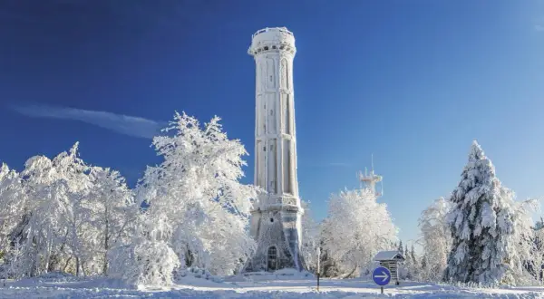 Tour de guet enneigée, tel un champ du feu blanc sous un ciel bleu intense. Arbres givrés et paysage hivernal.