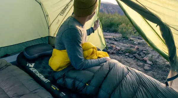 Un campeur, dans sa tente, tient un sac de couchage jaune. Il est temps de savoir comment ranger un sac de couchage pour le prochain voyage.