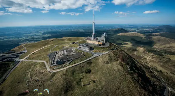Vue aérienne du Puy de Dôme dans le Massif Central, avec sa tour de télécommunication et des parapentistes profitant du paysage.