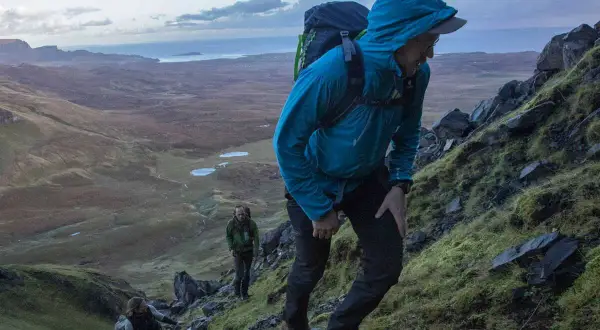 Randonneurs sur un sentier escarpé du Skye Trail, profitant d'un paysage spectaculaire avec des lacs et la mer en arrière-plan.