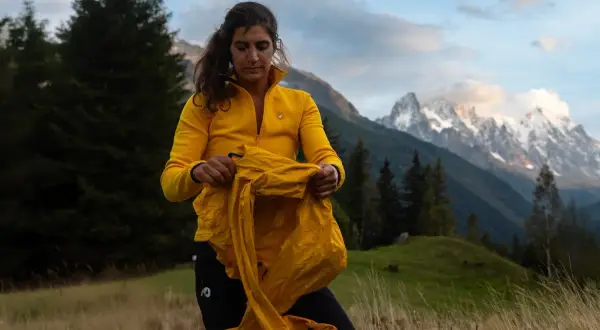 Une randonneuse en jaune prépare ses affaires, prête pour une aventure en montagne. Ses 3 couches randonnée sont essentielles pour affronter le climat changeant.