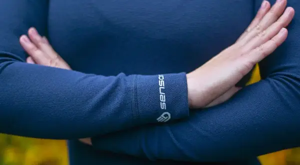 Une personne porte un pull bleu marine en laine mérinos, doux et chaud. Le logo "Sensor" est visible sur le poignet.