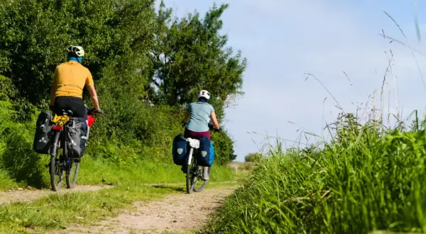 Deux cyclistes explorent un chemin de terre bordé d'arbres et d'herbes hautes. Le soleil brille, un décor idyllique pour le meilleur endroit pour faire du vélo en France.