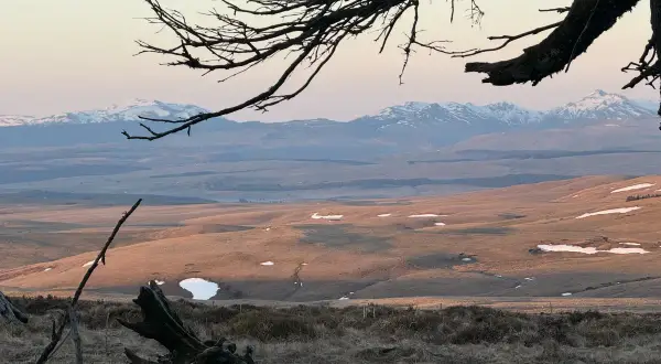 Vue panoramique depuis le Signal du Luguet, avec des montagnes enneigées à l'horizon et des collines dorées par le soleil couchant.