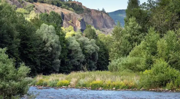 Rivière paisible traversant la gorge de l'Allier, bordée de végétation luxuriante et de falaises rocheuses.