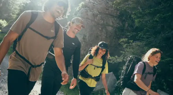Quatre randonneurs souriants avancent sur un sentier. Le poids du sac à dos en randonnée semble léger pour ce groupe joyeux.