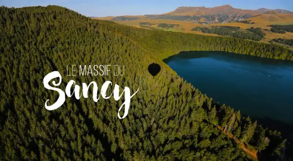 Vue aérienne du lac Estivadoux, niché au cœur du Massif du Sancy, avec une ombre de montgolfière sur la forêt.
