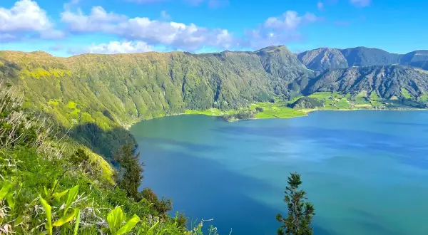 Vue panoramique sur le lac d'une beauté saisissante à São Miguel, entouré de montagnes verdoyantes sous un ciel bleu éclatant.