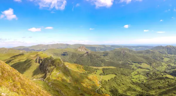 Magnifique panorama du Puy Mary, avec ses crêtes verdoyantes et ses vallées boisées sous un ciel bleu éclatant.